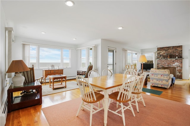 dining space with a brick fireplace, light hardwood / wood-style floors, and a baseboard heating unit