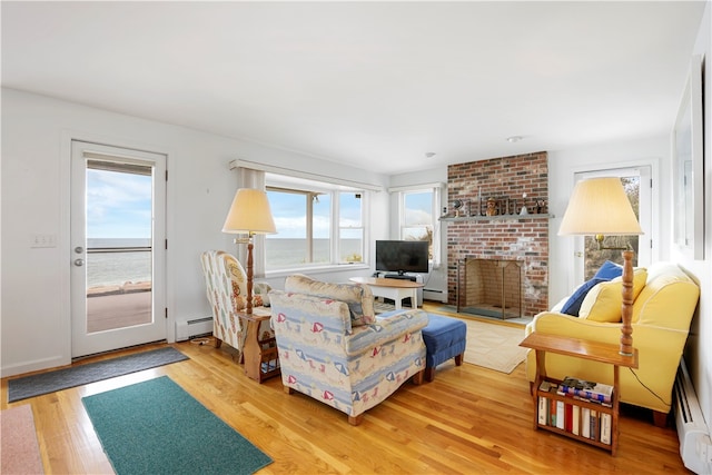 living room featuring a baseboard radiator, wood-type flooring, a water view, and a brick fireplace