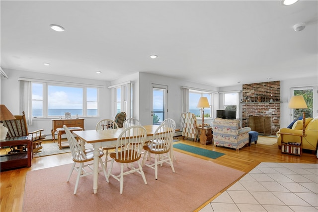 dining room featuring a fireplace, light wood-type flooring, and a water view