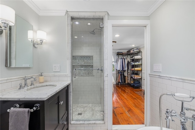 bathroom with tile walls, wood-type flooring, walk in shower, ornamental molding, and vanity