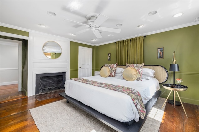 bedroom featuring ornamental molding, dark wood-type flooring, ceiling fan, and a large fireplace