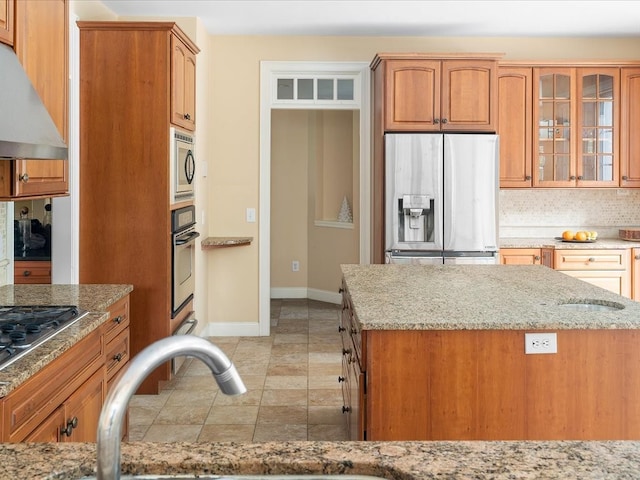 kitchen featuring backsplash, light stone countertops, stainless steel appliances, range hood, and sink