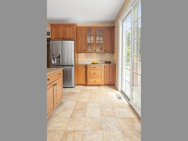 kitchen featuring light stone counters, backsplash, stainless steel refrigerator with ice dispenser, and plenty of natural light