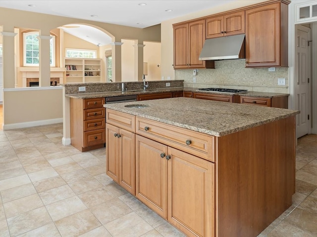 kitchen with tasteful backsplash, a kitchen island, stone countertops, stainless steel gas stovetop, and decorative columns