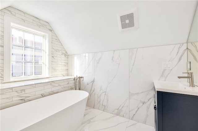 bathroom with vanity, a tub to relax in, vaulted ceiling, and tile walls