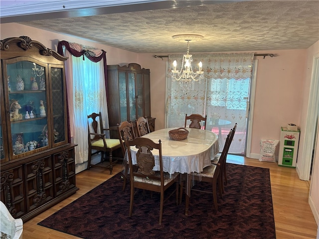 dining space with a textured ceiling, light hardwood / wood-style floors, and an inviting chandelier