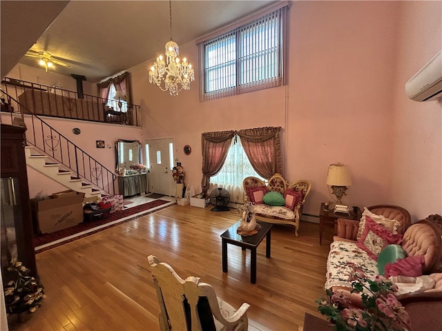 living room featuring ceiling fan with notable chandelier, a high ceiling, a wall mounted AC, hardwood / wood-style floors, and a baseboard heating unit