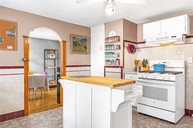 kitchen with white gas range, tile walls, range hood, and white cabinets