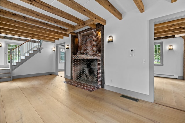 unfurnished living room with light hardwood / wood-style flooring, a baseboard heating unit, beam ceiling, and plenty of natural light