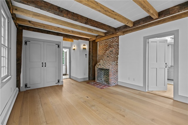 unfurnished living room featuring beamed ceiling, light hardwood / wood-style flooring, a fireplace, and a baseboard heating unit