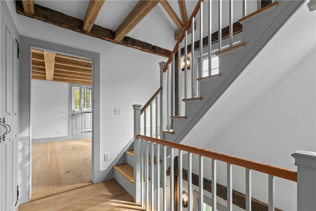 staircase featuring wood-type flooring and beamed ceiling