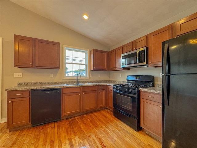 kitchen featuring light stone counters, sink, black appliances, light wood-type flooring, and vaulted ceiling