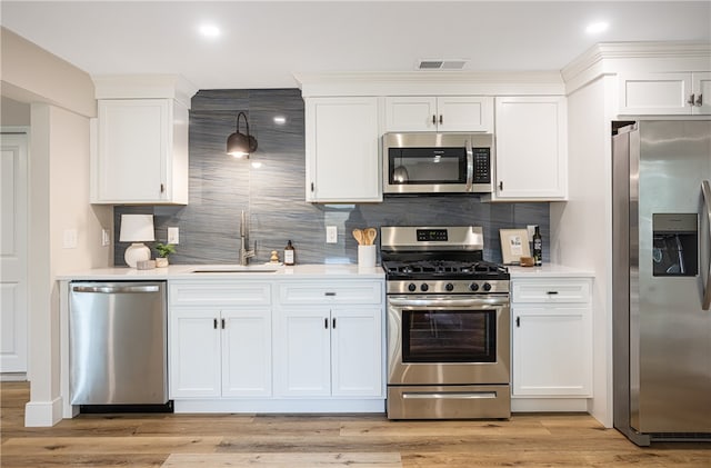 kitchen with appliances with stainless steel finishes, light wood-type flooring, white cabinetry, and sink