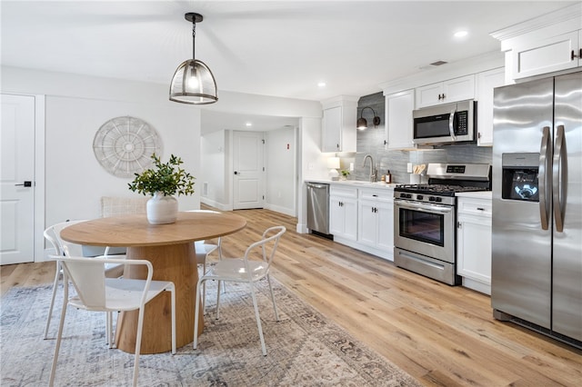 kitchen with appliances with stainless steel finishes, decorative light fixtures, light hardwood / wood-style flooring, and white cabinets