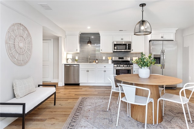 kitchen featuring white cabinets, light hardwood / wood-style floors, appliances with stainless steel finishes, and hanging light fixtures