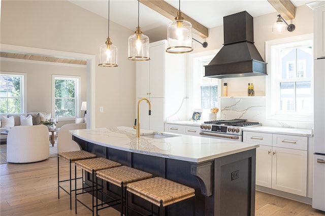 kitchen featuring premium range hood, high end stove, white cabinetry, and an island with sink