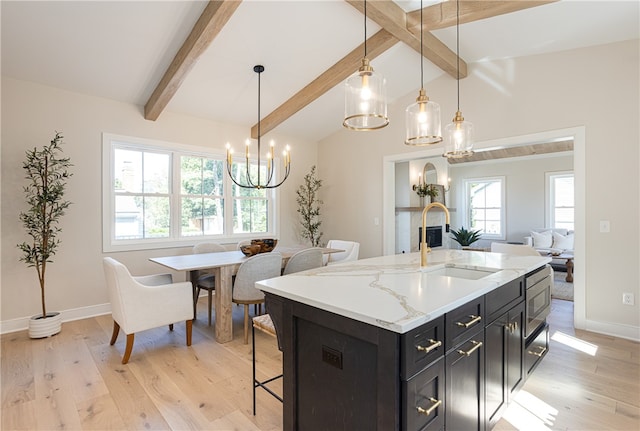 kitchen with light wood-type flooring, hanging light fixtures, a kitchen island with sink, and a wealth of natural light