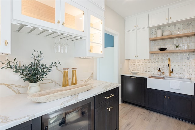 bar featuring sink, beverage cooler, white cabinetry, light stone countertops, and light hardwood / wood-style floors