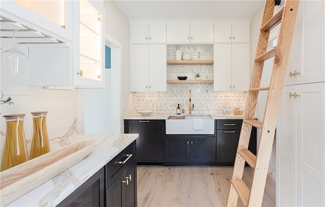 bar featuring light stone counters, tasteful backsplash, sink, white cabinets, and light hardwood / wood-style flooring