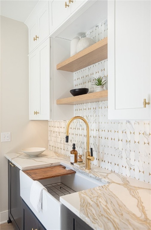 interior details featuring light stone counters, white cabinets, sink, and decorative backsplash