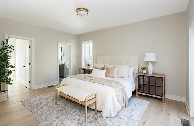 bedroom with connected bathroom and light hardwood / wood-style floors