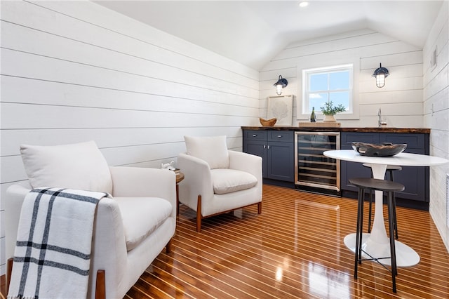 living area with wooden walls, vaulted ceiling, beverage cooler, and dark hardwood / wood-style flooring