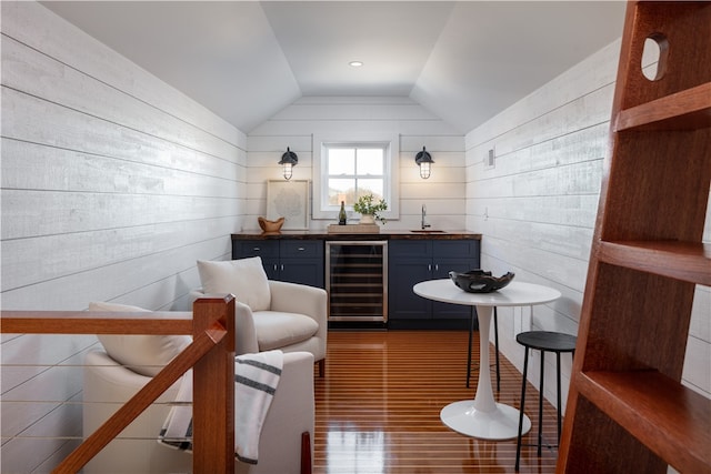 bar with lofted ceiling, wood walls, sink, beverage cooler, and dark wood-type flooring