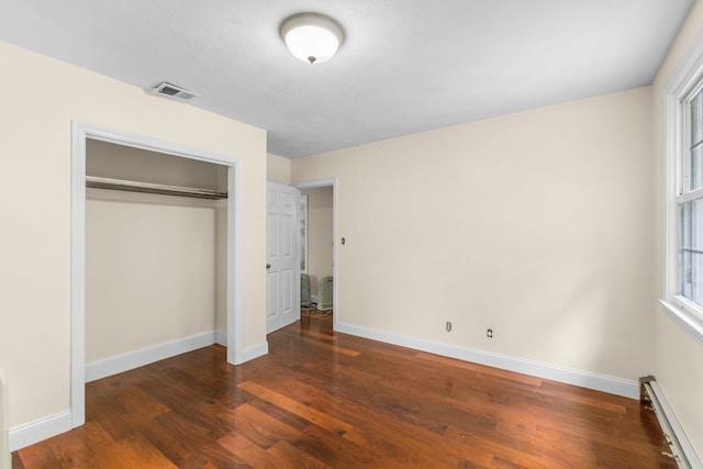 unfurnished bedroom with a closet, baseboard heating, and dark hardwood / wood-style flooring