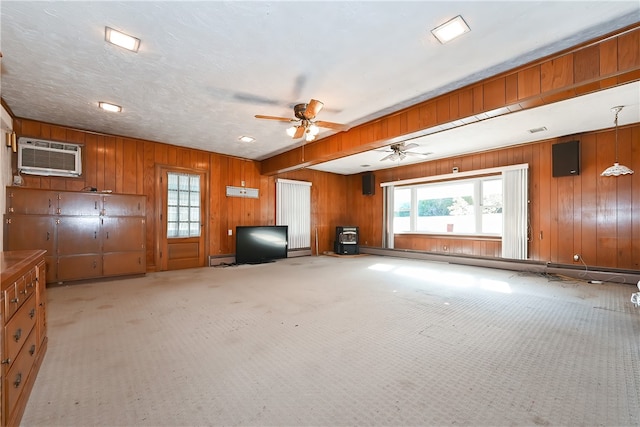 unfurnished living room with a wall unit AC, wood walls, light colored carpet, and ceiling fan