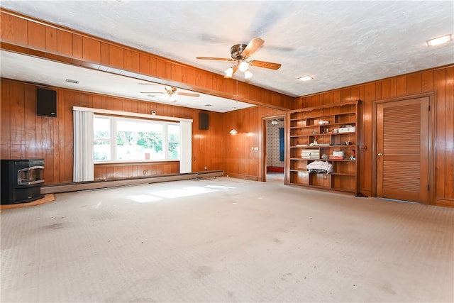 unfurnished living room featuring carpet flooring, a wood stove, baseboard heating, and wooden walls