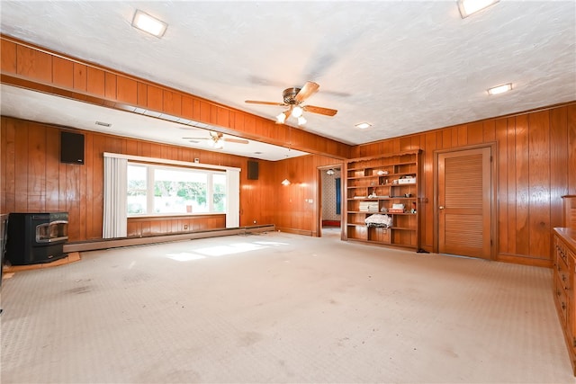 unfurnished living room featuring baseboard heating, wooden walls, and a wood stove