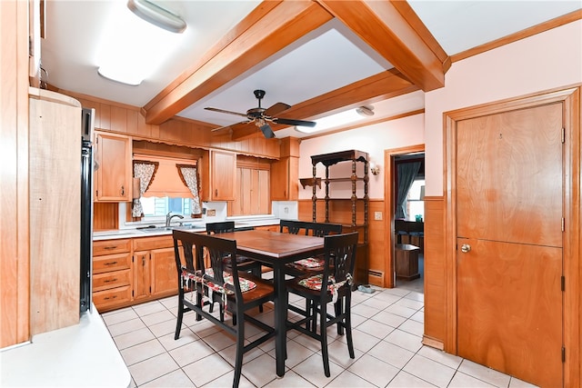 tiled dining space featuring a baseboard radiator, sink, ceiling fan, wooden walls, and beam ceiling