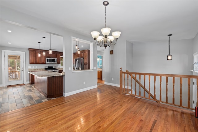 kitchen featuring kitchen peninsula, light wood-type flooring, pendant lighting, a notable chandelier, and stainless steel appliances