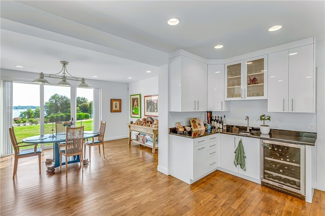 kitchen featuring light wood-type flooring, wine cooler, white cabinetry, and decorative light fixtures