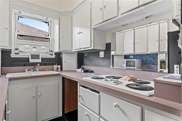 kitchen with white stovetop, backsplash, sink, and white cabinetry