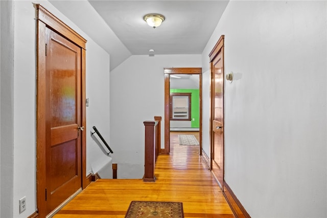 hallway with light hardwood / wood-style floors, vaulted ceiling, and a baseboard radiator