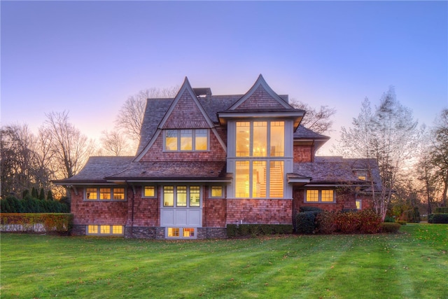 back house at dusk featuring a lawn