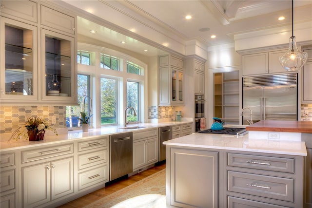 kitchen with tasteful backsplash, sink, hanging light fixtures, appliances with stainless steel finishes, and ornamental molding