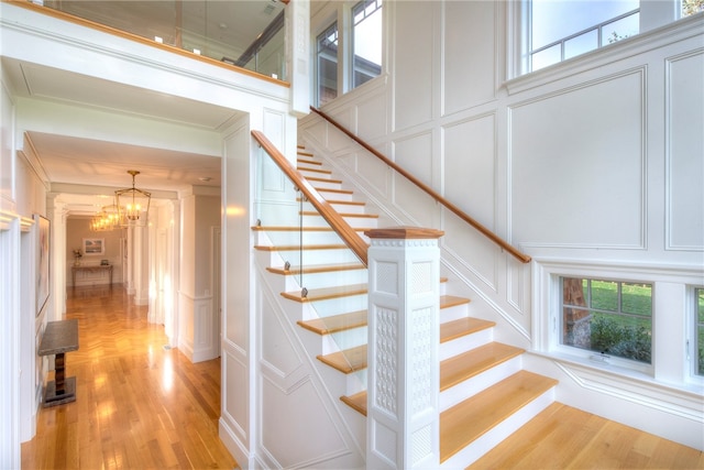 staircase featuring a towering ceiling, a chandelier, hardwood / wood-style floors, and crown molding