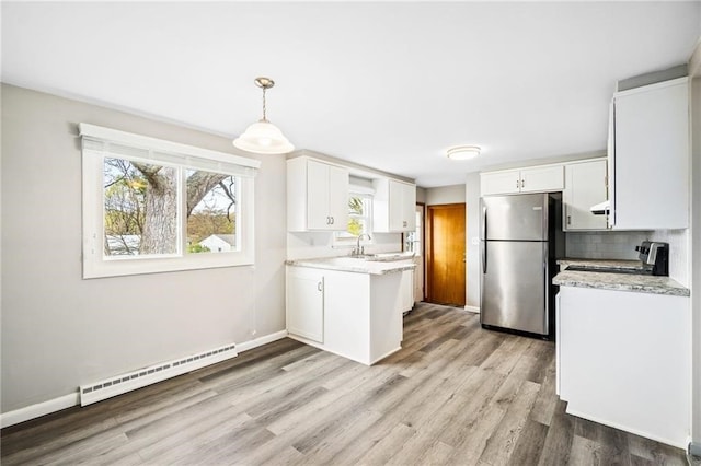 kitchen with baseboard heating, appliances with stainless steel finishes, white cabinets, and decorative light fixtures