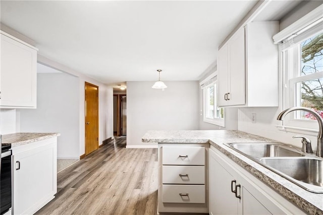 kitchen with white cabinetry, kitchen peninsula, decorative light fixtures, and light wood-type flooring