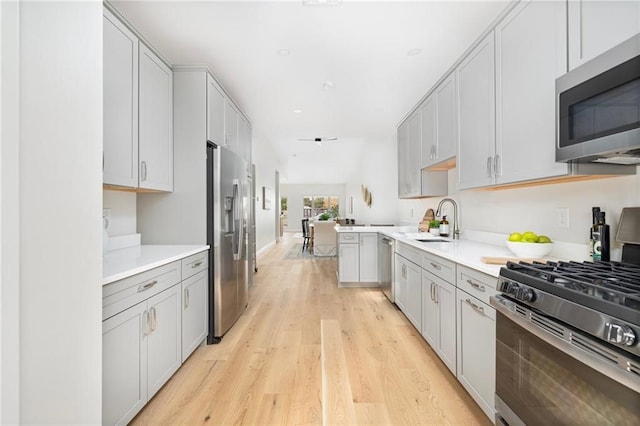 kitchen featuring sink, kitchen peninsula, stainless steel appliances, and light wood-type flooring