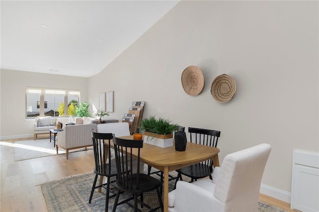 dining room featuring high vaulted ceiling and light hardwood / wood-style flooring