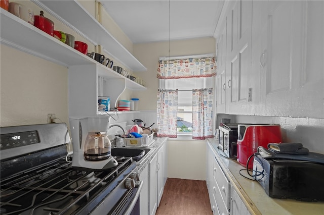 kitchen featuring gas range, sink, hardwood / wood-style floors, and white cabinetry