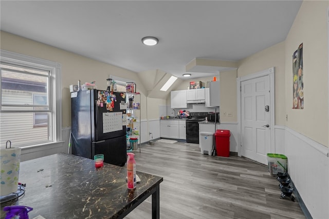 kitchen featuring vaulted ceiling with skylight, dark stone counters, black appliances, hardwood / wood-style flooring, and white cabinetry