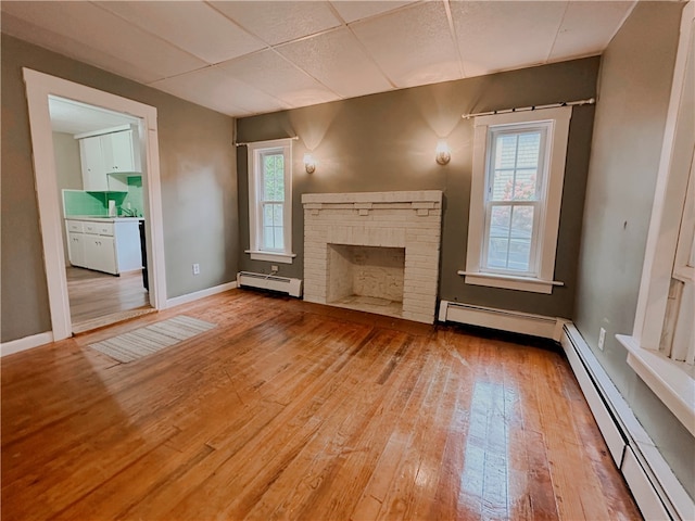 unfurnished living room featuring a baseboard heating unit, wood-type flooring, and a healthy amount of sunlight