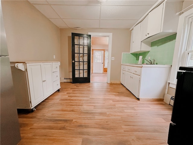 kitchen with baseboard heating, a drop ceiling, light wood-type flooring, white cabinets, and tasteful backsplash