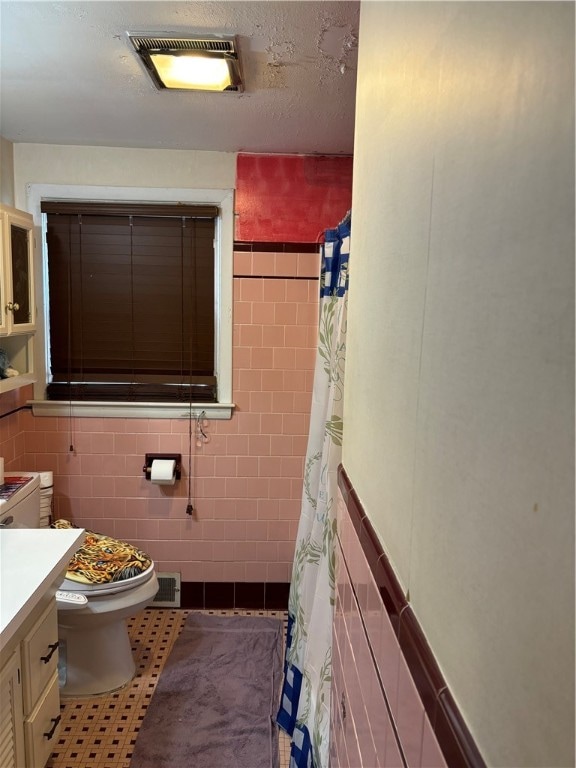 bathroom featuring vanity, tile walls, tile patterned floors, toilet, and a textured ceiling