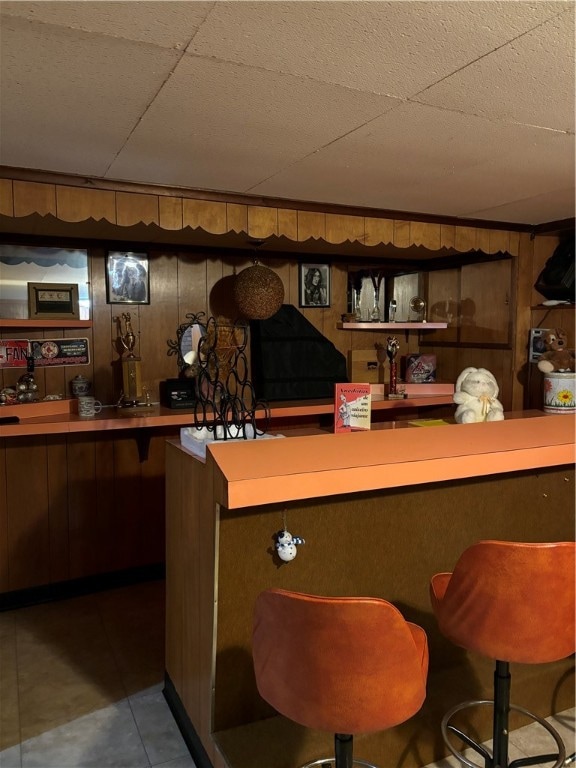 bar featuring a drop ceiling and wooden walls