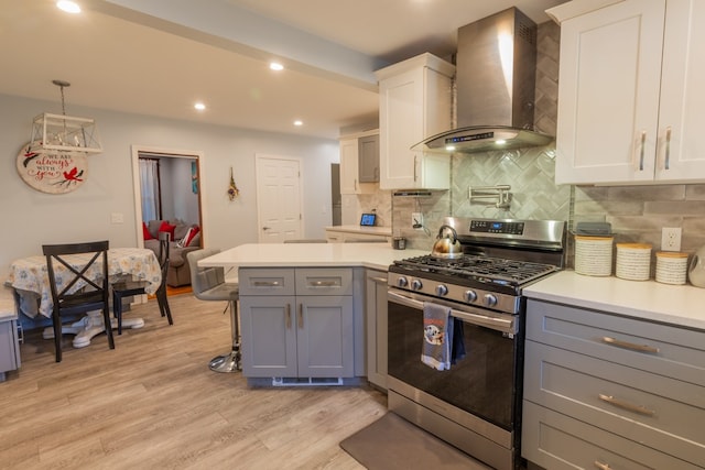 kitchen featuring light wood-type flooring, white cabinets, stainless steel gas stove, wall chimney range hood, and gray cabinets